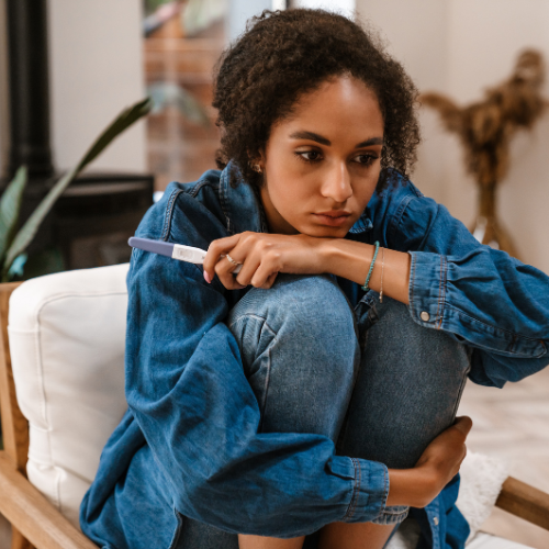 A young woman sitting quietly with a pregnancy test, lost in thought